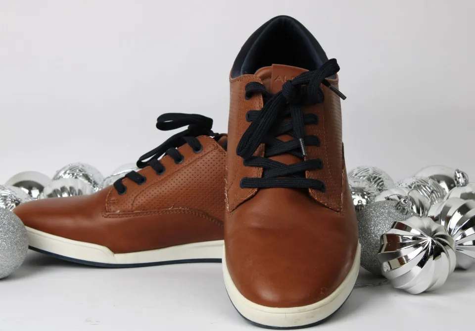 Elegantes zapatos de piel marrón con cordones negros, adornados con ornamentos navideños plateados.